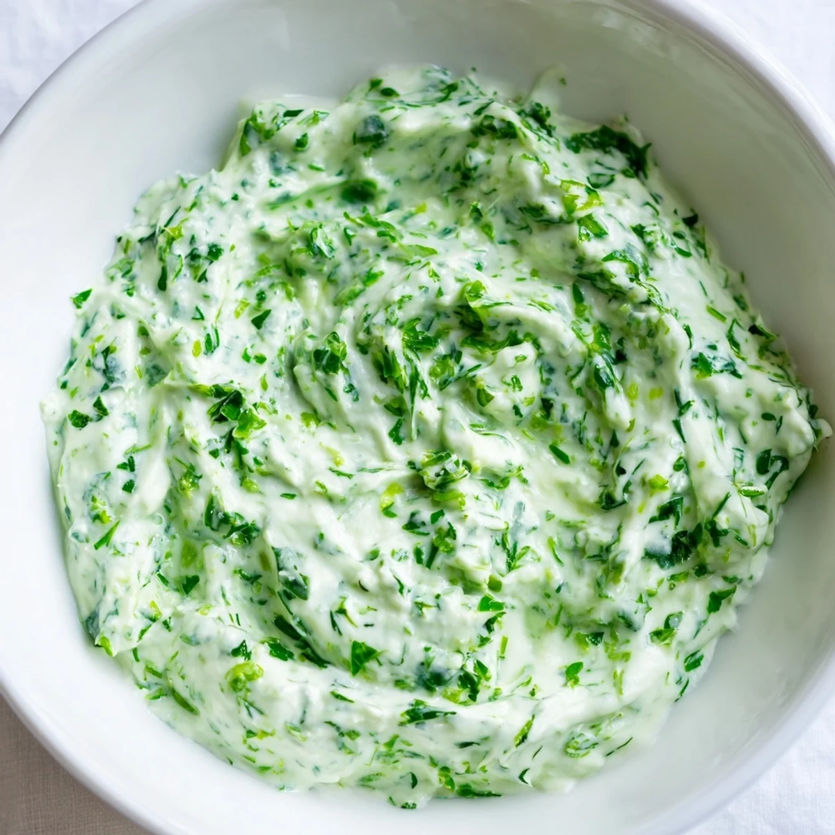 Homemade Green Goddess Salad Dip garnished with parsley and chives, ready to be scooped up with carrot sticks and tortilla chips.