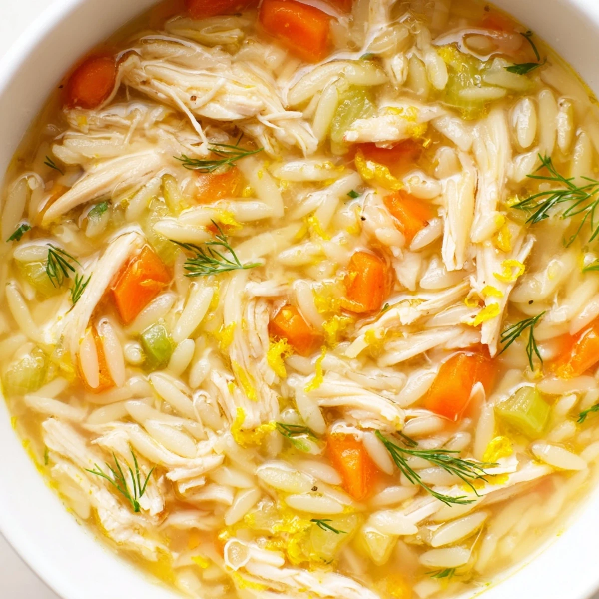 A close-up bowl of steaming Chicken Lemon Orzo Soup, garnished with fresh dill and lemon slices, ready to serve.