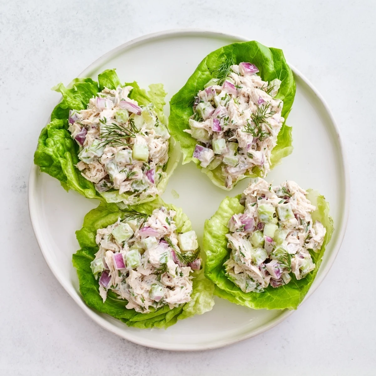 Fresh dill pickle chicken salad scooped into vibrant green lettuce cups, showcasing creamy texture.  