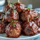 A platter of tender Grape Jelly and Chili Sauce Meatballs served with toothpicks, alongside a bowl of extra sweet and tangy sauce.  