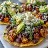 Sliced avocado and crumbled feta top these easy Black Bean and Sweet Potato Tostadas served on a plate.