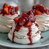 Mini pavlovas with strawberries and cream: crisp meringue shells topped with whipped cream and juicy berries.