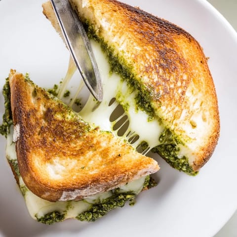 A delicious Spinach Pesto Grilled Cheese sandwich on a rustic cutting board, garnished with fresh basil leaves and served alongside a bowl of creamy tomato soup.