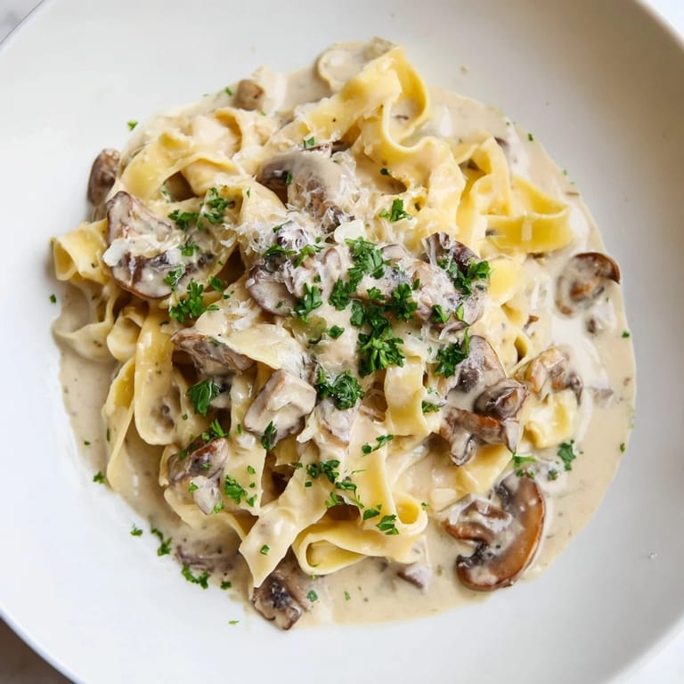 Tightly shot of a pan of creamy mushroom Alfredo, highlighting the velvety sauce and sautéed mushrooms.  