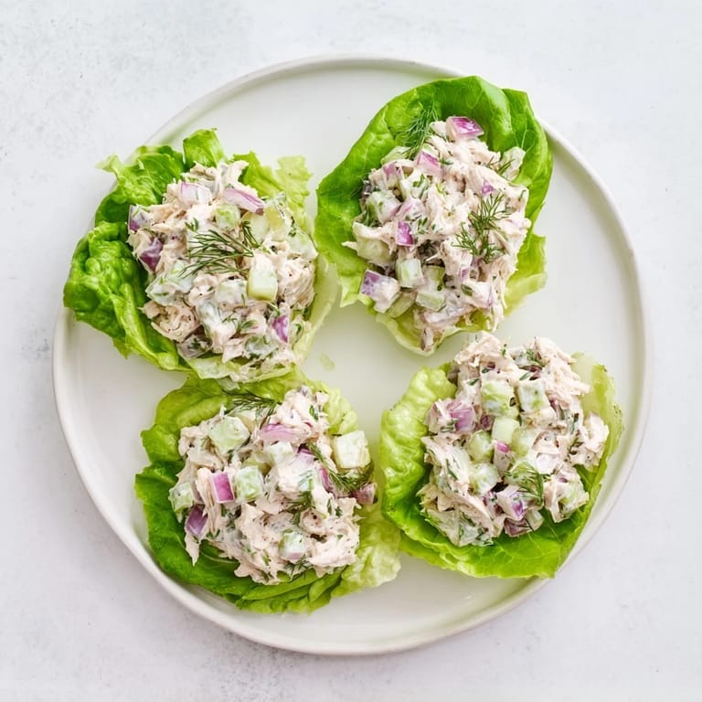 Fresh dill pickle chicken salad scooped into vibrant green lettuce cups, showcasing creamy texture.  